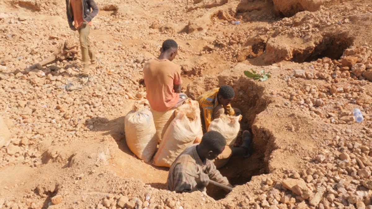 Boy in orange shirt on top of bags, boy in orange striped shirt holding bag, boy in light brown flannel digging for cobalt in the ground in Democratic Republic of the Congo