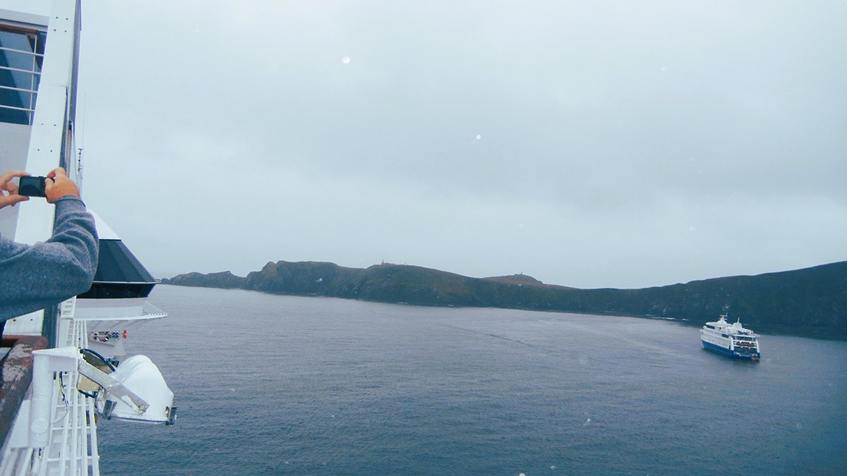 Person taking a photo of Cape Horn, Chile as a ship goes by in the distance