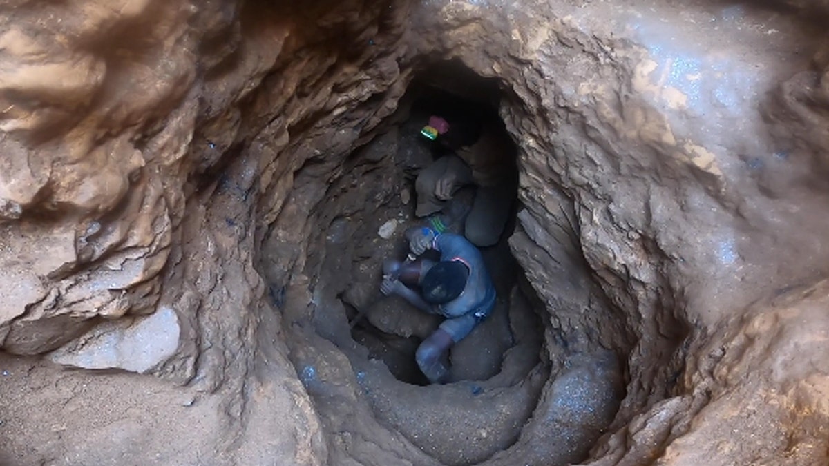 Boy in blue shirt and shorts and another person digging in a mine for cobalt in Democratic Republic of the Congo