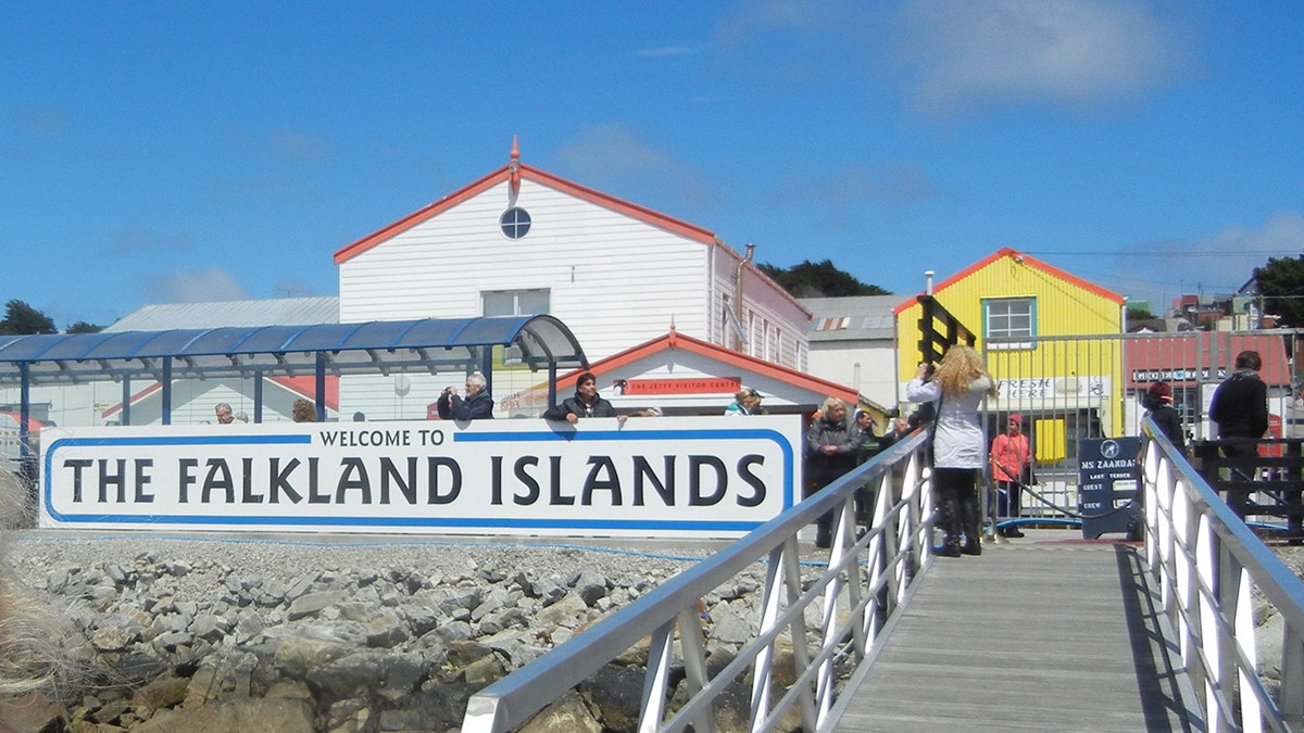 Falkland Islands sign in front of a pair of buildings, people on footpath