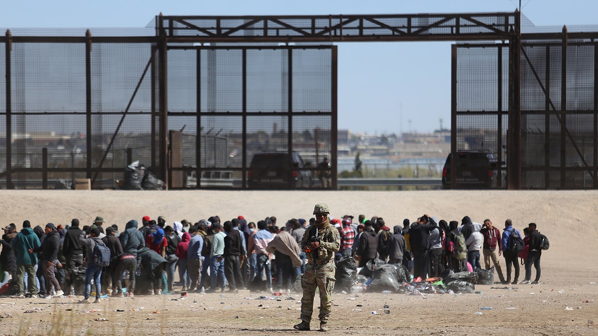 Migrants and a border official near the border wall