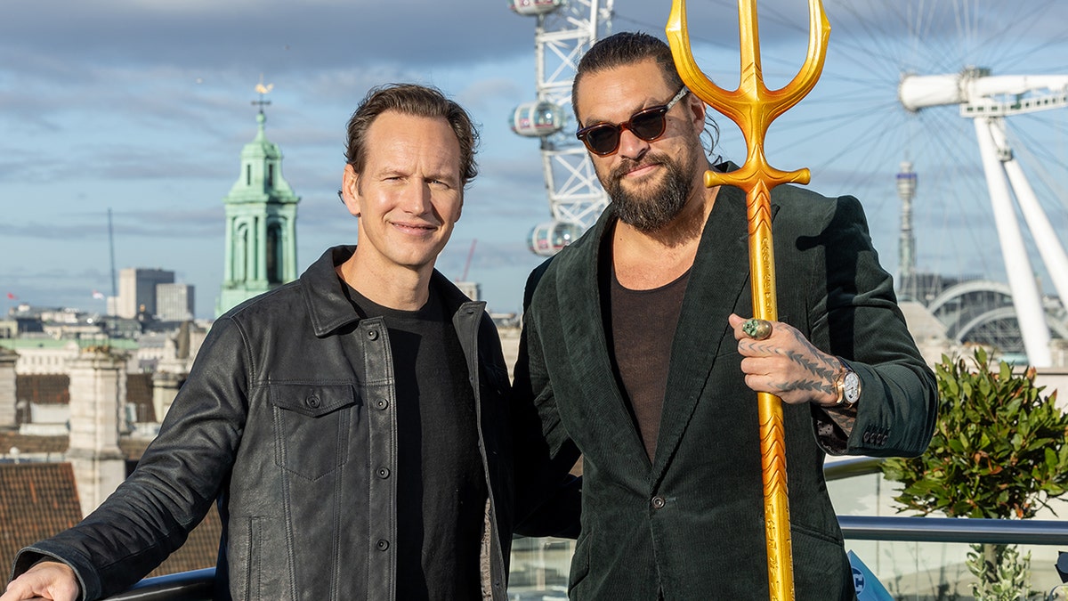 Patrick Wilson in a black shirt and jacket and Jason Momoa holding a triden in a green velvet suit attend a carpet event for the "Aquaman"