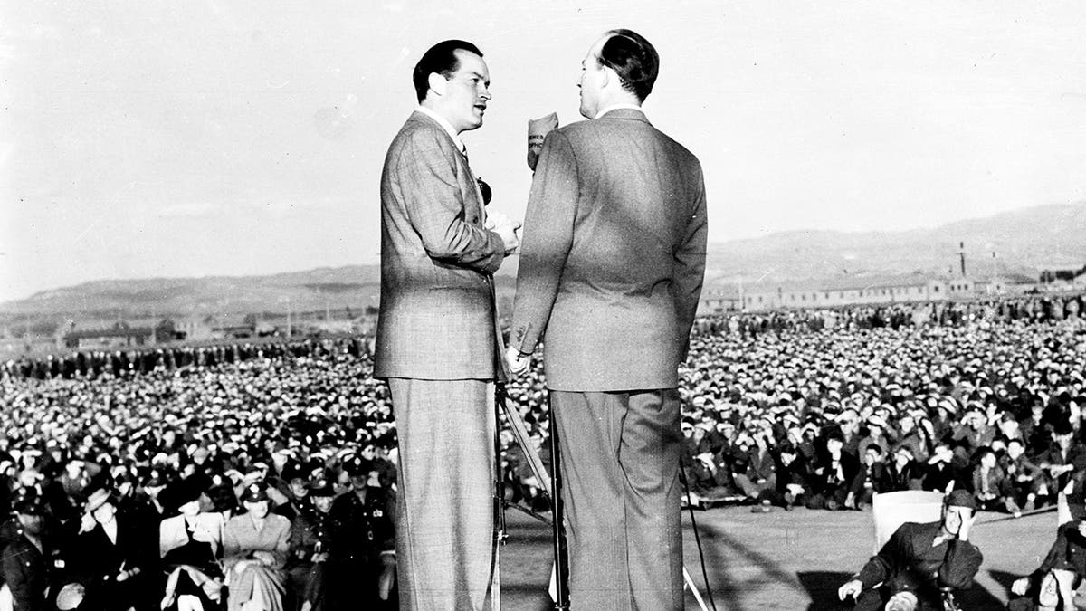 Bob Hope and Bing Crosby with their backs facing the camera as they sing to US troops
