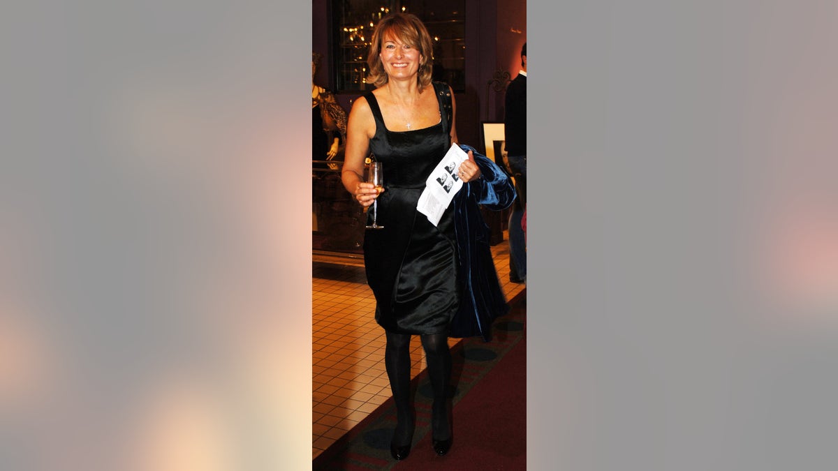 Carole Middleton wearing a black strappy dress while holding a champagne flute and a pamplet