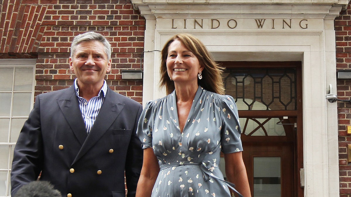 Carole Middleton in a polka dot blue dress smiling ouside the hospital with her husband Michael