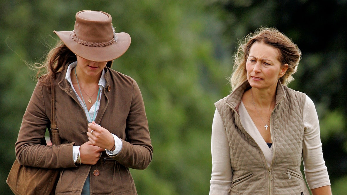 Kate Middleton keeps her head down in a brown hat as her mother looks at her sternly
