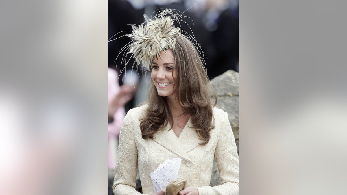 Kate Middleton wearing a feathered fascinator and a matching ivory dress