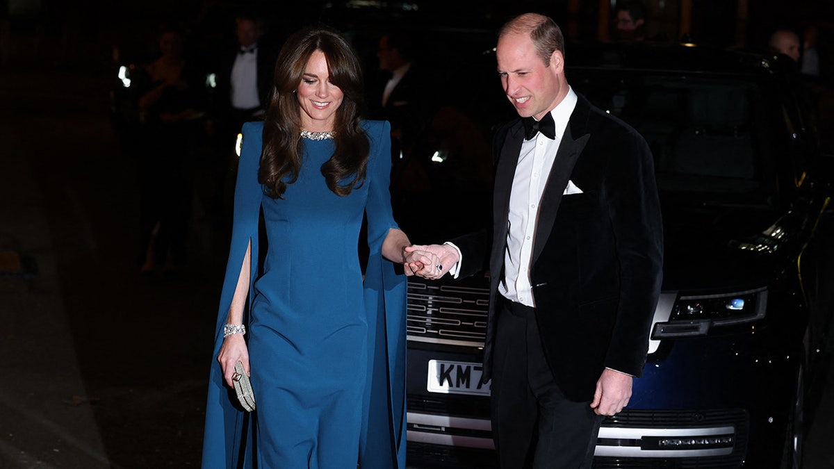 Prince WIlliam holding Kate Middleton's hand as they both wear formal attire for an evening appearance