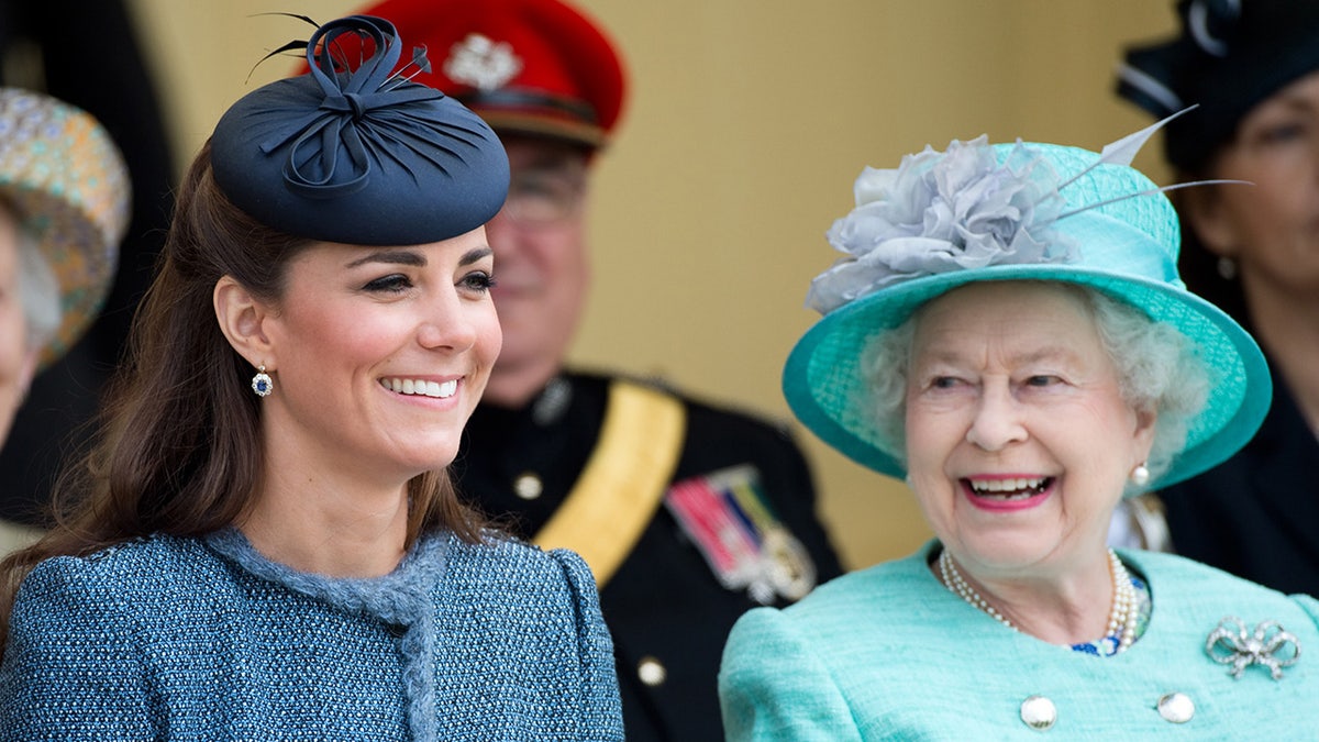 Kate Middleton smiling sitting next to Queen Elizabeth II who is looking at her with admiration
