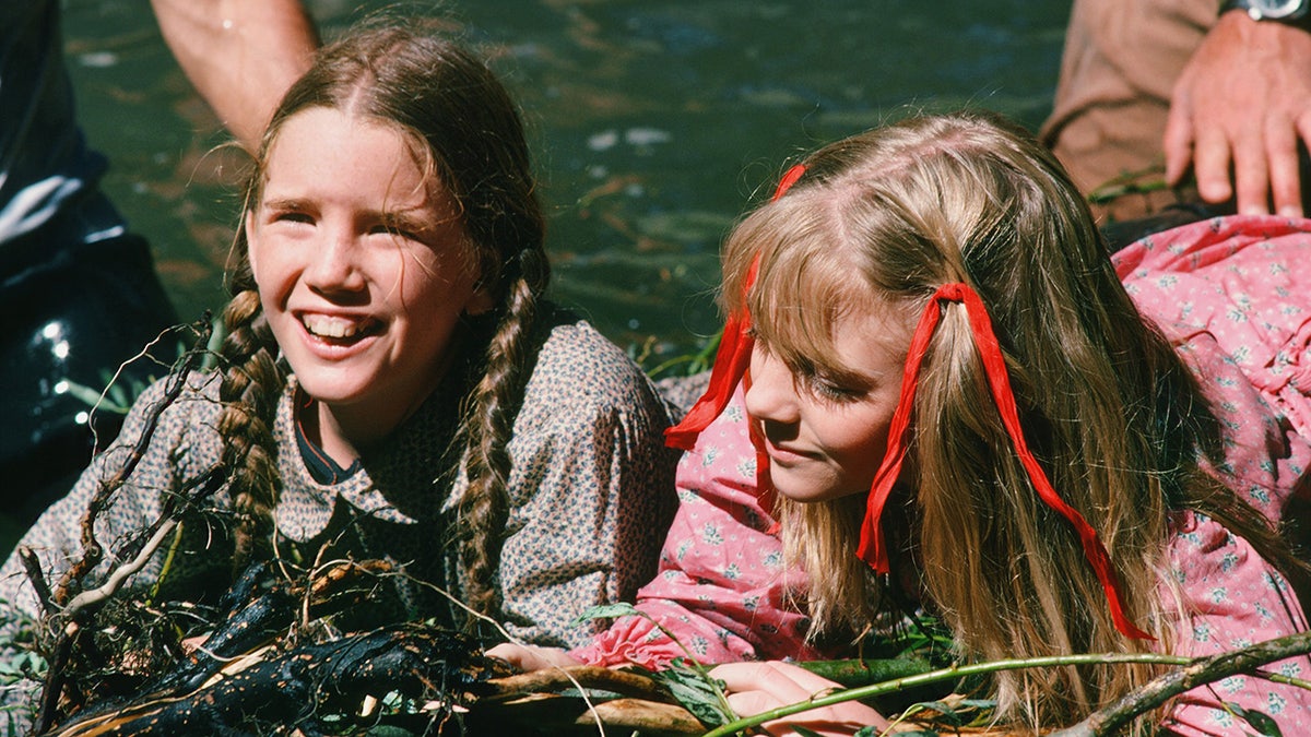 Melissa Gilbert and Alison Arngrim in character drenched in a pond