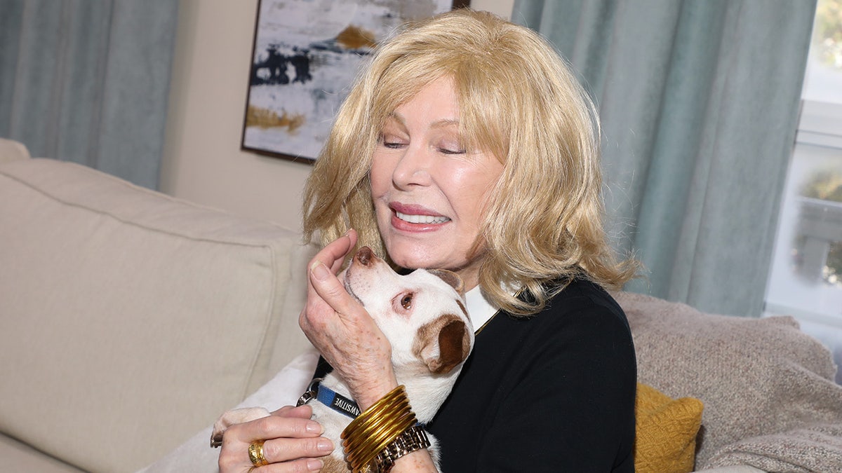 Loretta Swit smiling with her eyes closed as she embraces a small dog