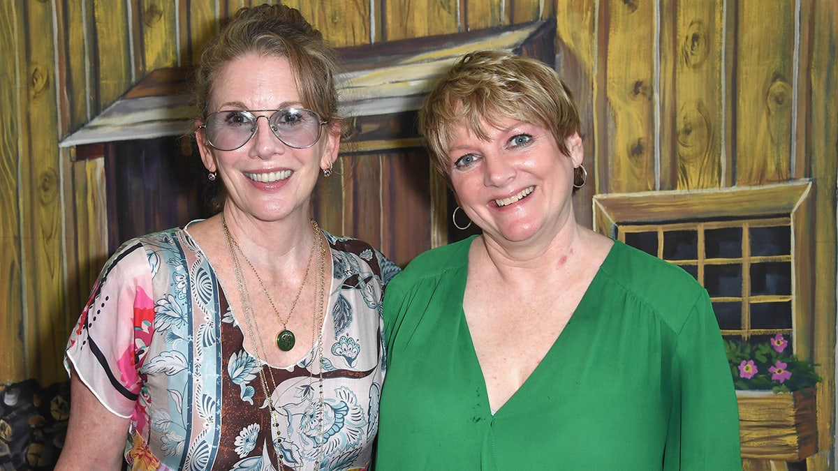 Alison Arngrim in a green dress next to Melissa Gilbert wearing a patterned dress and glasses