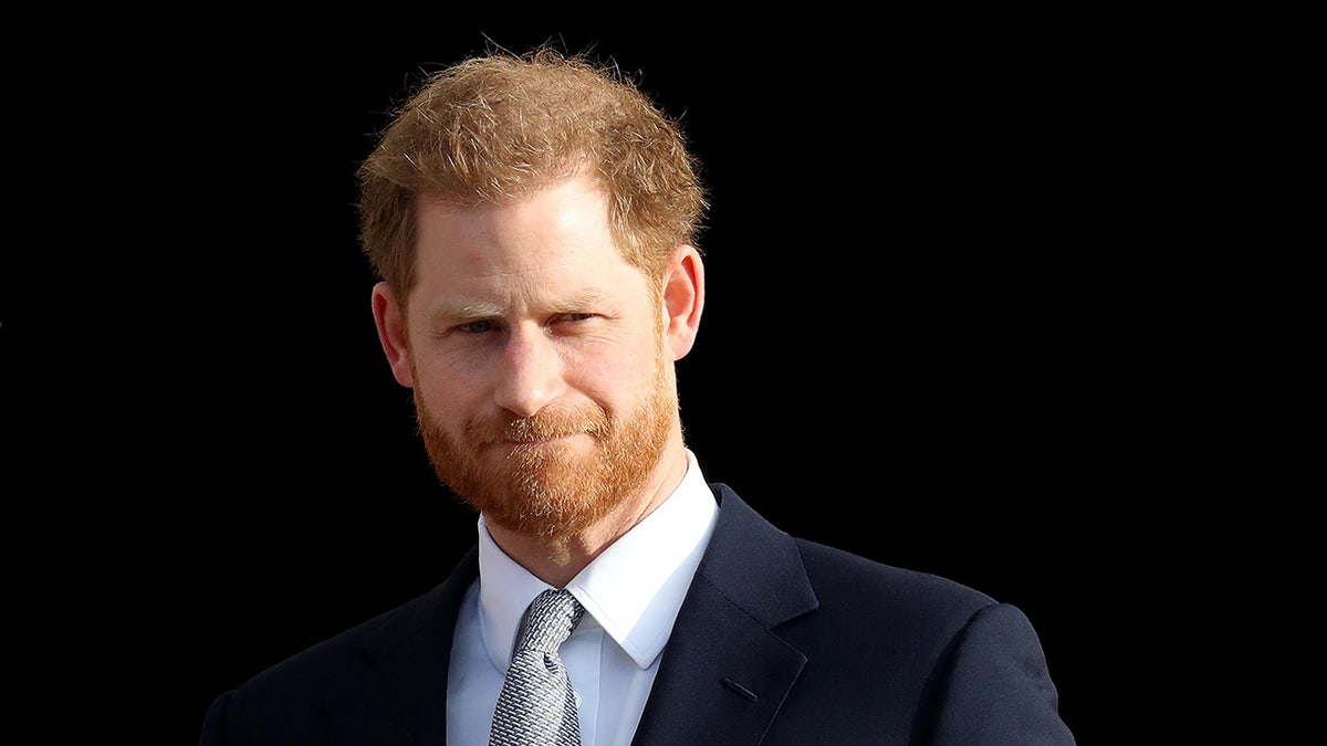 A close-up of Prince Harry in a suit against a black backdrop