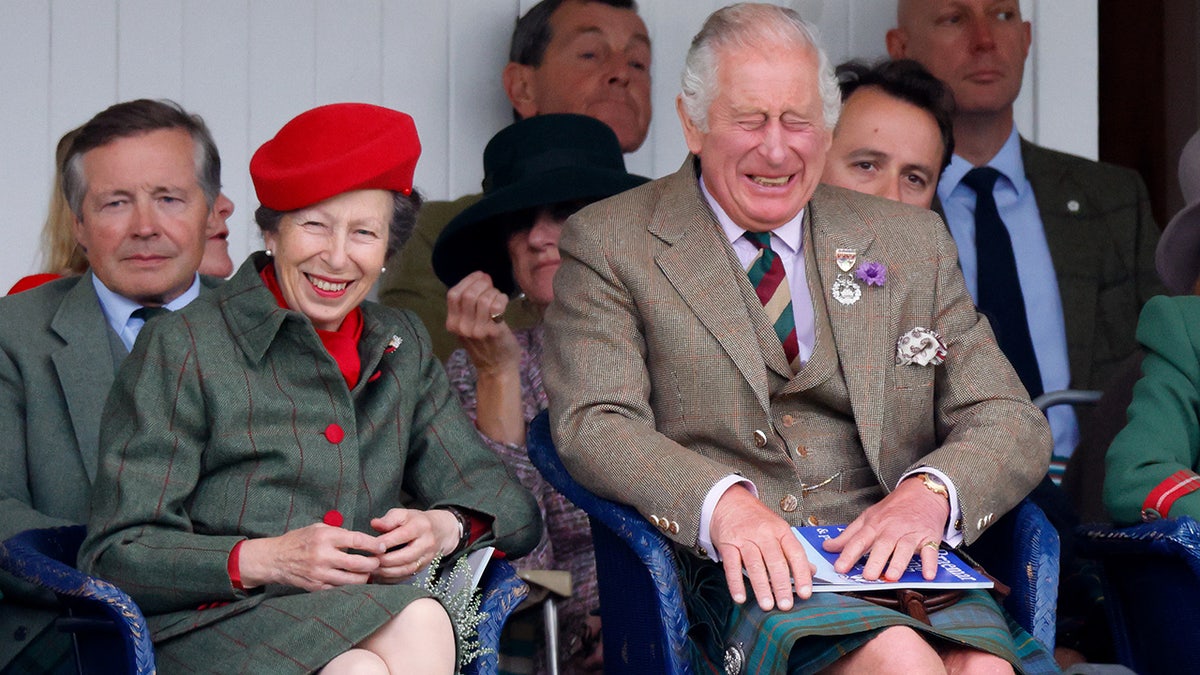 King Charles and Princess Anne sitting next to each other and laughing while wearing matching outfits