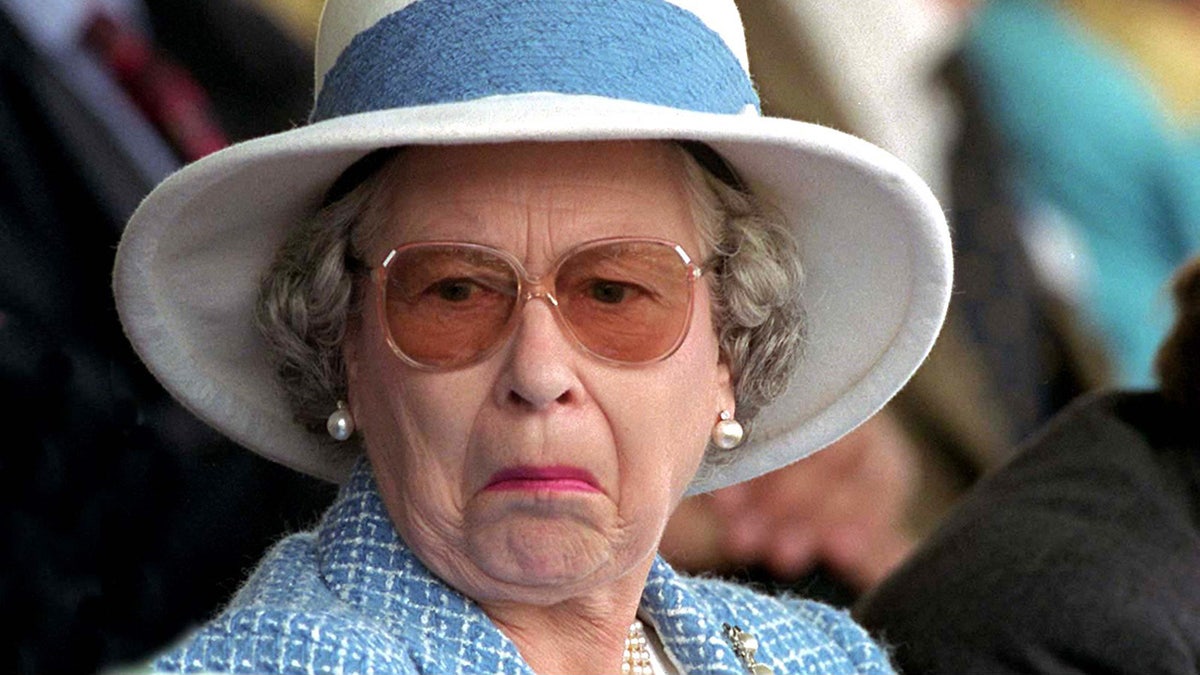 A close-up of Queen Elizabeth II making a funny face in a blue and white suit with a matching hat