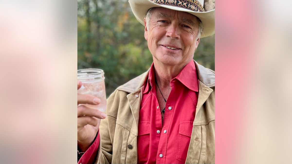 john schneider holding a glass of his moonshine