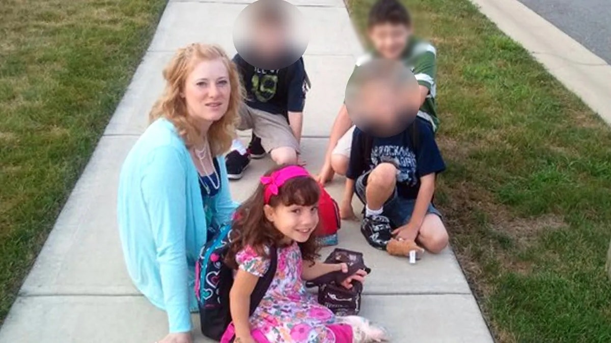 Kristine Barnett wearing a bright blue sweater sitting on the sidewalk with her children
