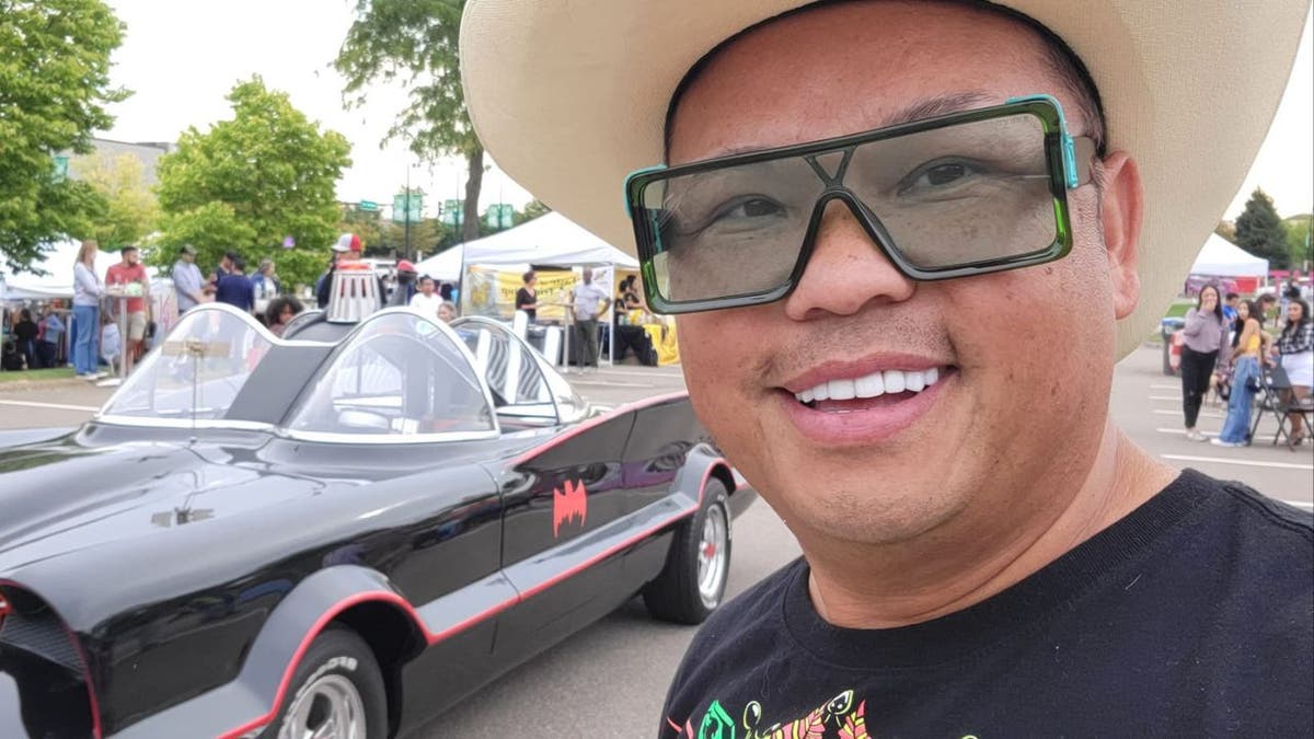 A selfie picture of Tou Ger Xiong, pictured, Tou Ger Xiong with an old batmobile