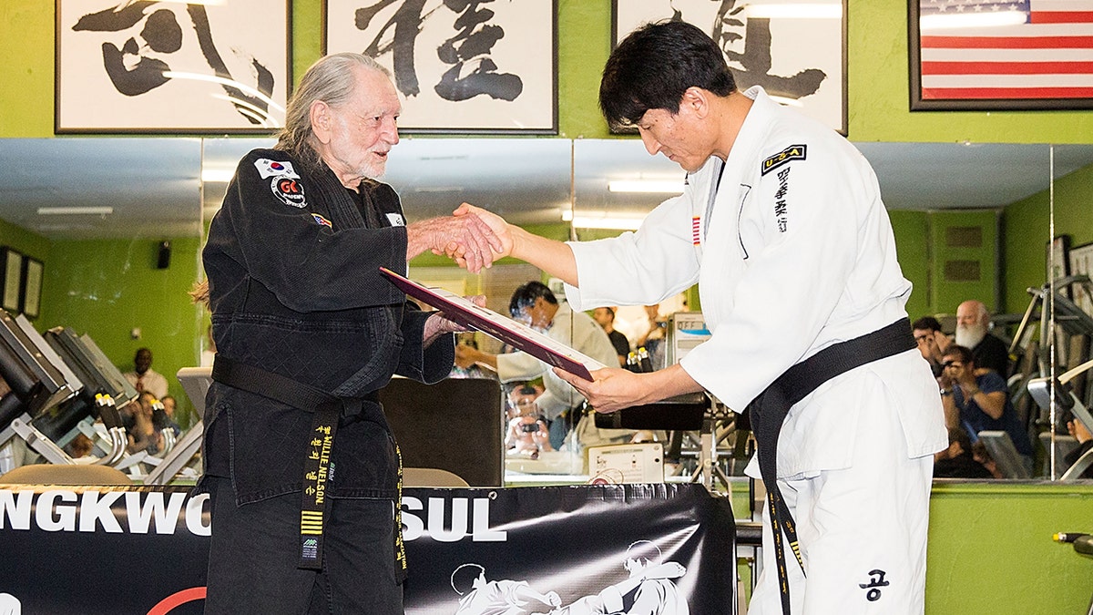 Willie Nelson receiving his 5th degree black belt honor from an instructor