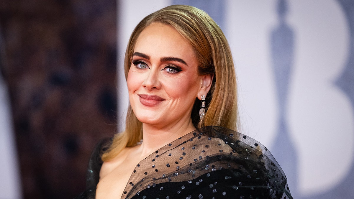 Adele sorri suavemente no tapete em um vestido preto profundo