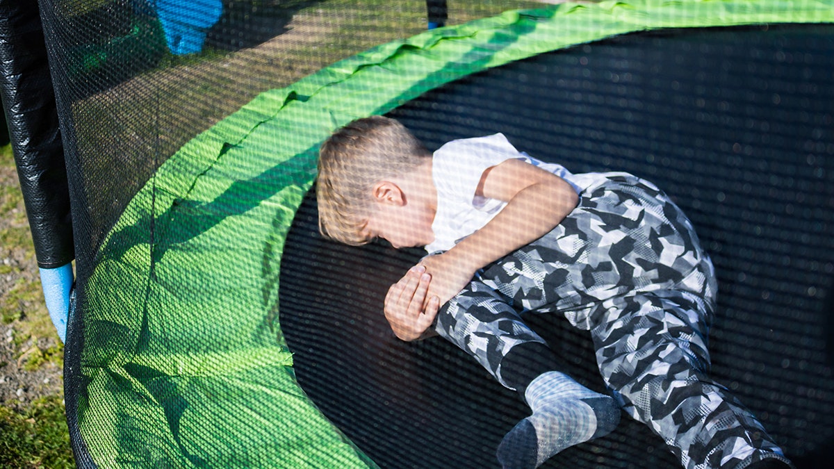 Little boy holding his knee in pain while jumping on trampoline.