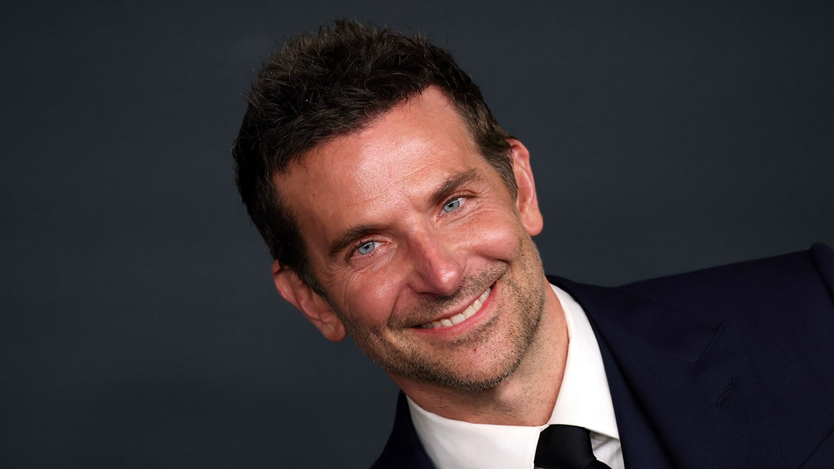 Bradley Cooper in a navy suit smiles on the carpet for "Maestro"