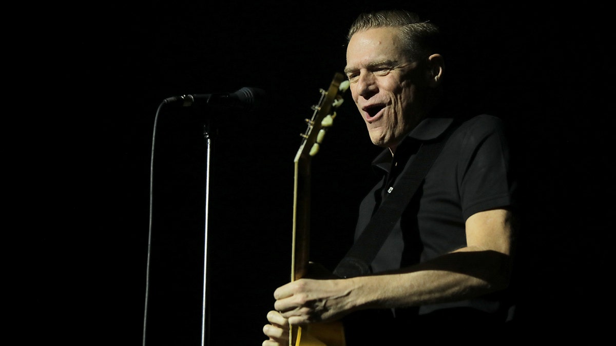 Bryan Adams side profile shot playing the guitar on stage