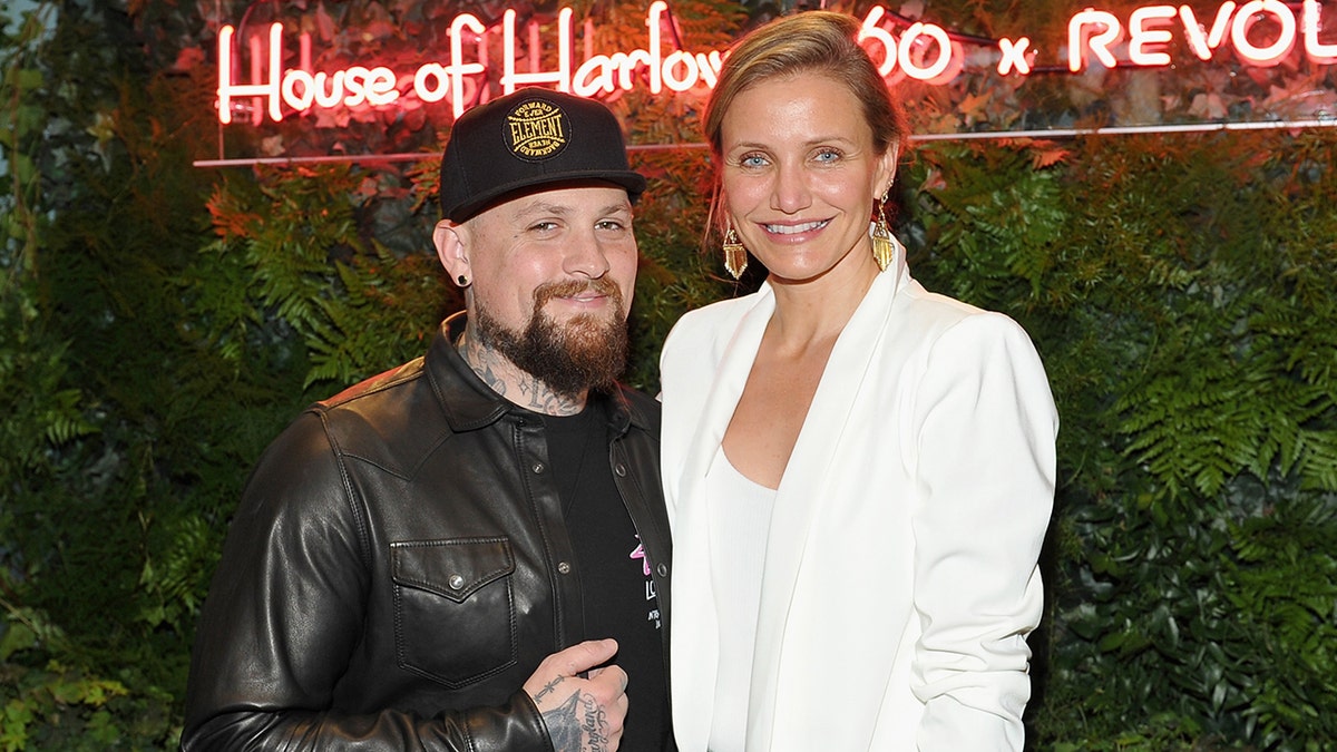 Benji Madden in a black leather jacket smiles with wife Cameron Diaz in a white blazer