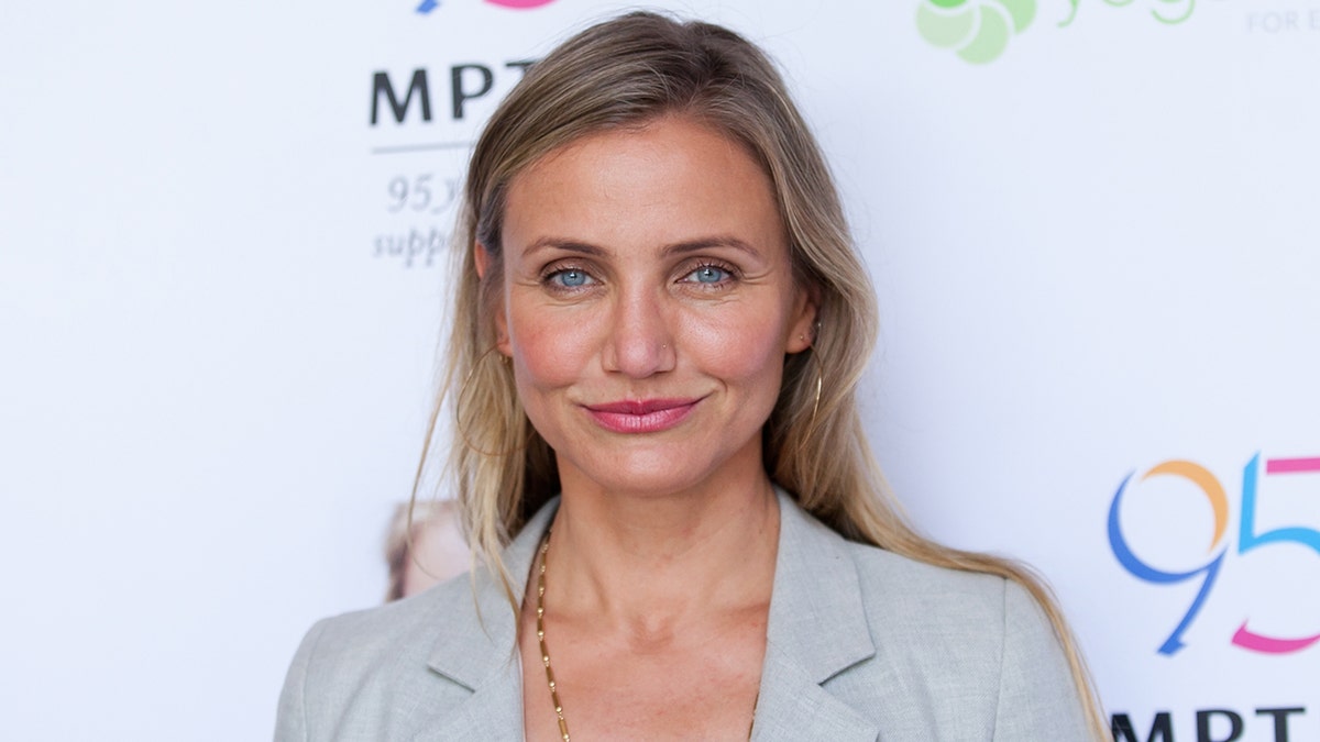 Cameron DIaz in a light blue and grey suit jacket soft smiles at an event