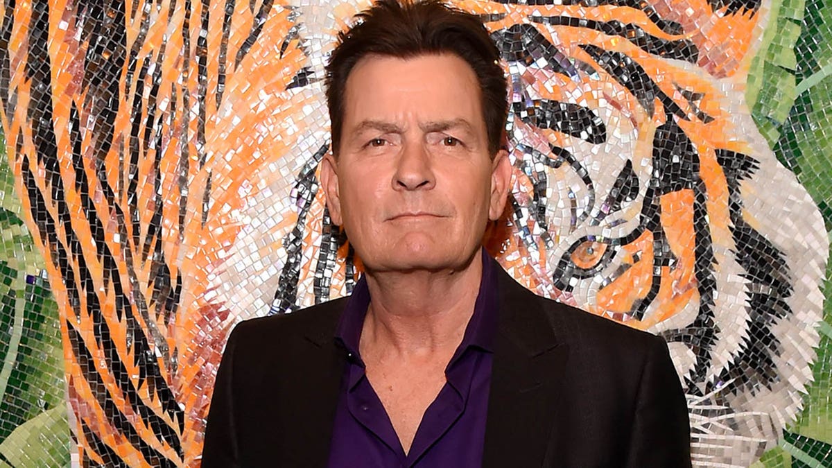charlie sheen looking at the camera in front of tiger wall background