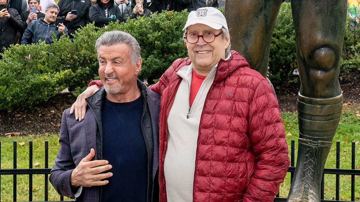 Chevy Chase hugs Sylvester Stallone in front of Rocky statue in Philadelphia