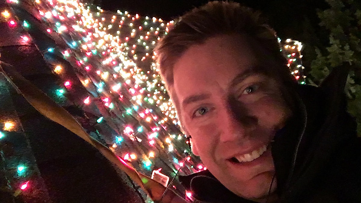 Jeremy Morris takes selfie on roof with glowing lights behind him