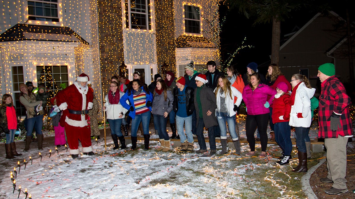 Carolers sing with Santa outside house with Christmas lights