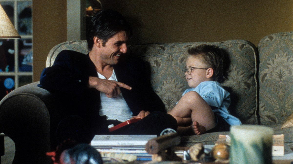 Tom Cruise and Jonathan Lipnicki sit on the couch and laugh during a scene from "Jerry Maguire"