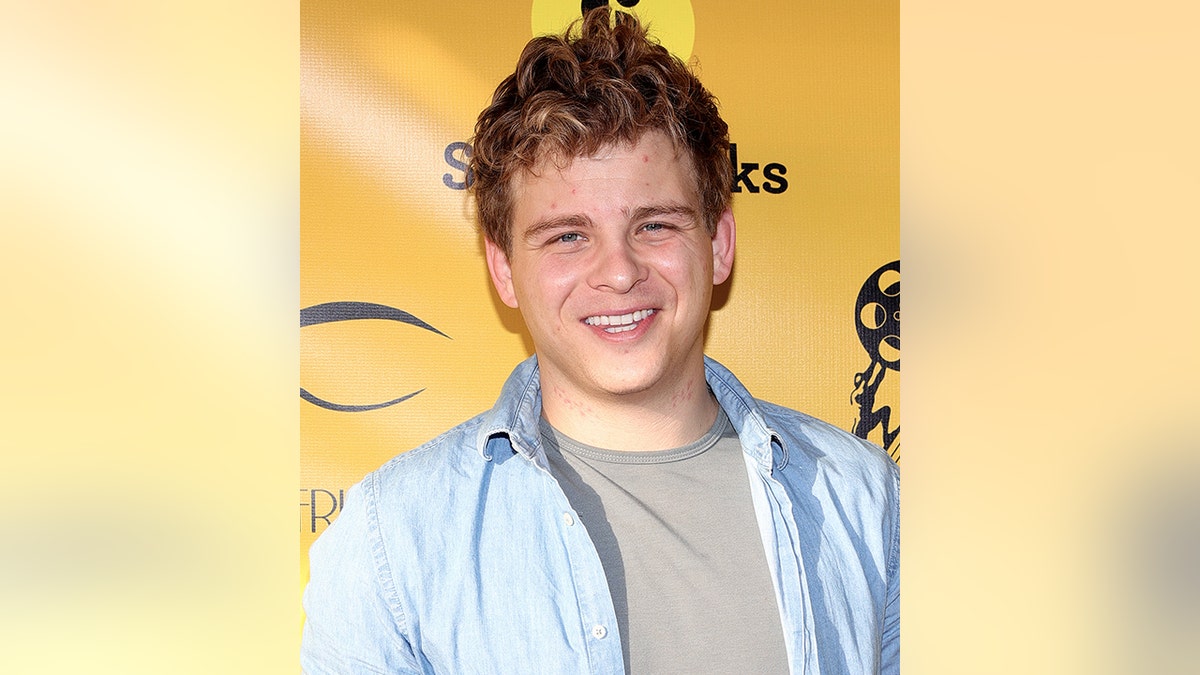 Jonathan Lipnicki smiles in a blue button down and grey t-shirt