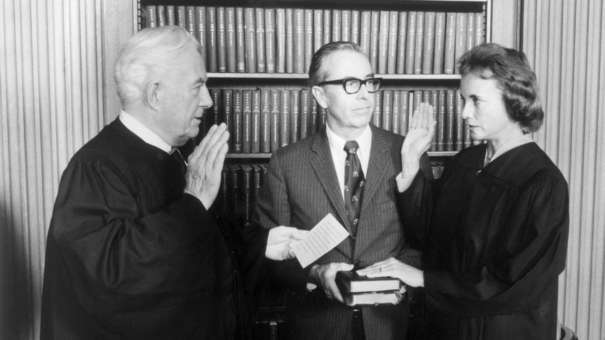 Justice O'Connor taking oath of office, right, while husband holds Bible