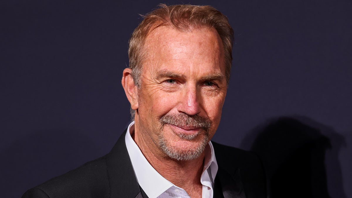 Kevin Costner smiles on red carpet wearing suit and shirt