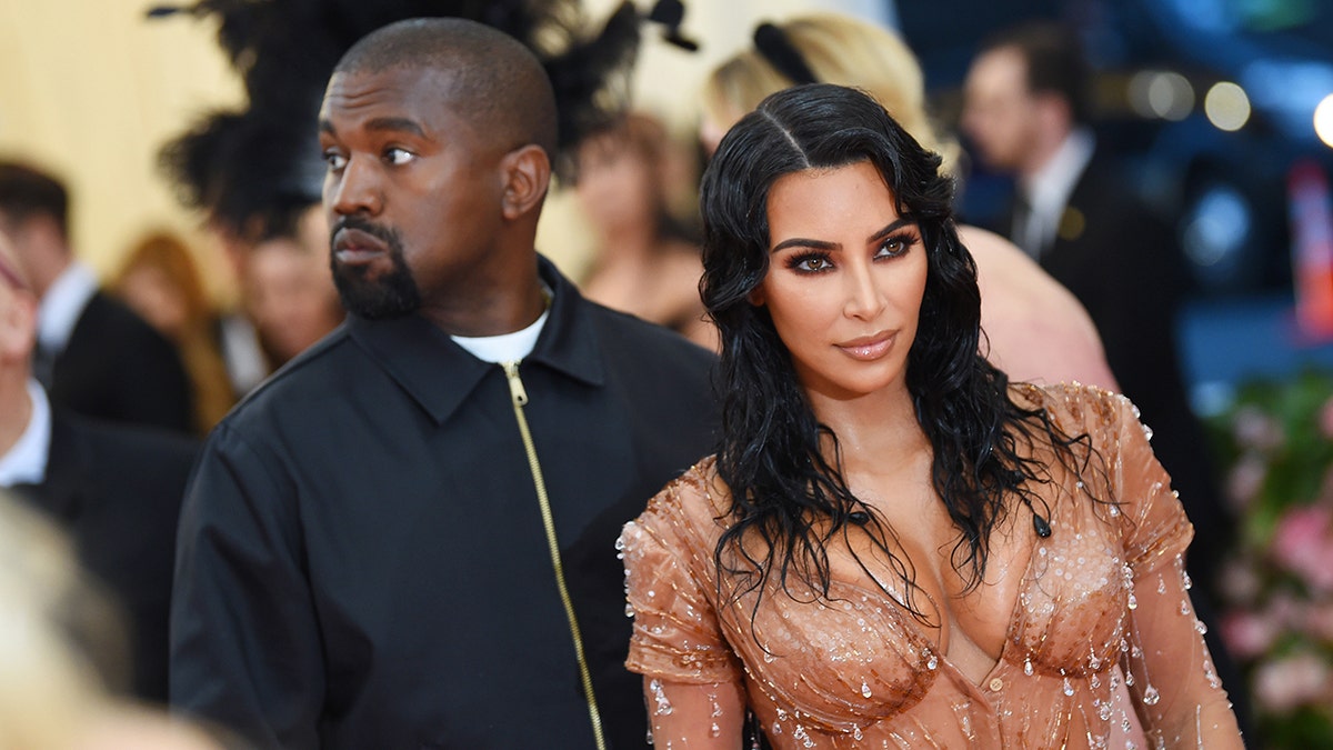 Kanye West in a bomber jacket looks away on the Met carpet with wife Kim Kardashian in a dripping bodycon dress