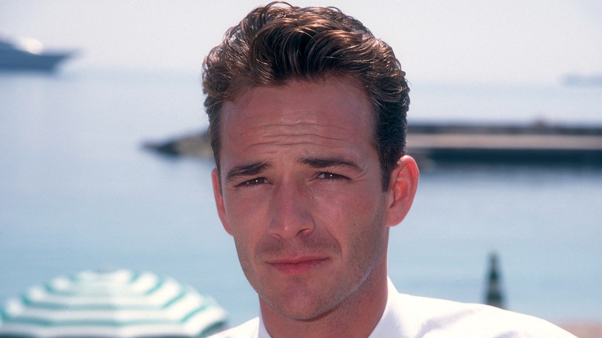 A young Luke Perry in a white shirt with Monte Carlo in the background