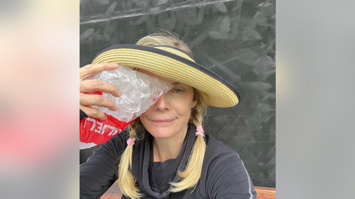 Michelle Pfeiffer, com cabelo trançado e chapéu de palha no topo, segura um saco de gelo no rosto após uma lesão no pickleball