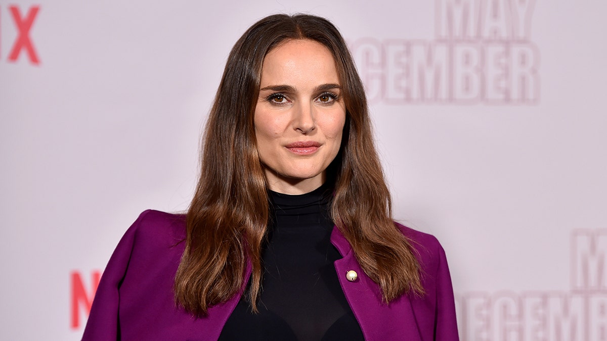 Natalie Portman in a bright plum purple jacket and black turtleneck on the carpet