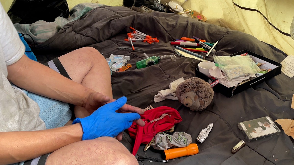 Inside of homeless woman's tent with needles, foil, DVD case and other items