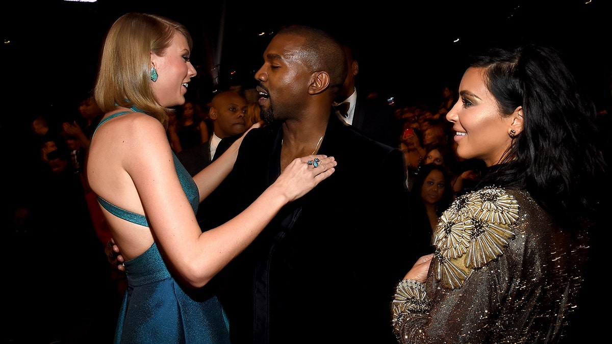 Taylor Swift in a teal dress hugs Kanye West in black at the 2015 Grammy Awards with Kim Kardashian