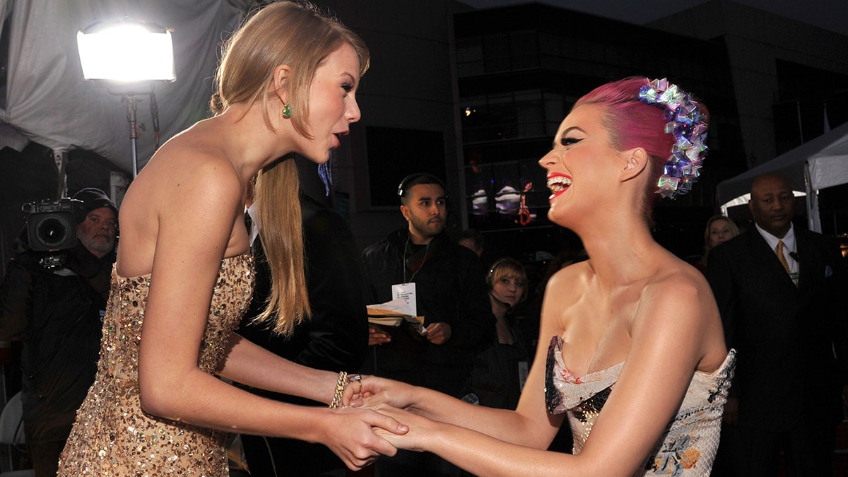 Taylor Swift in gold holds onto Katy Perry's hands who has pink hair at the American Music Awards