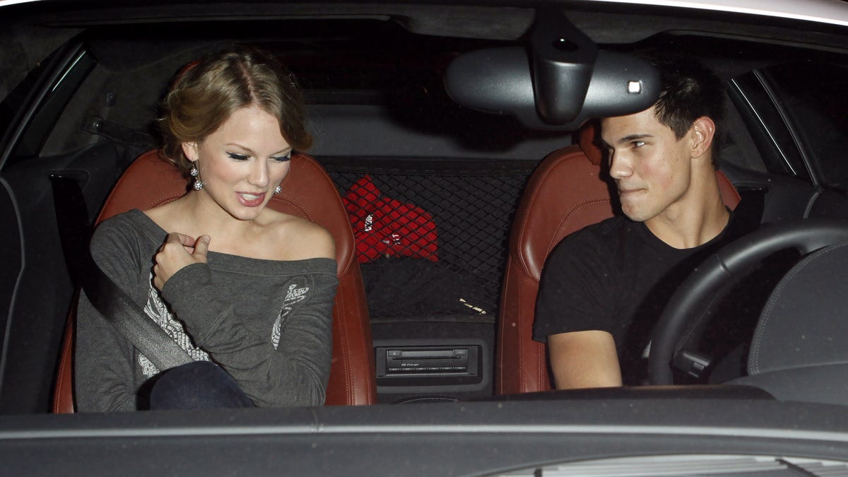 Taylor Swift looks down and laughs as Taylor Lautner looks at her and drives her in his car