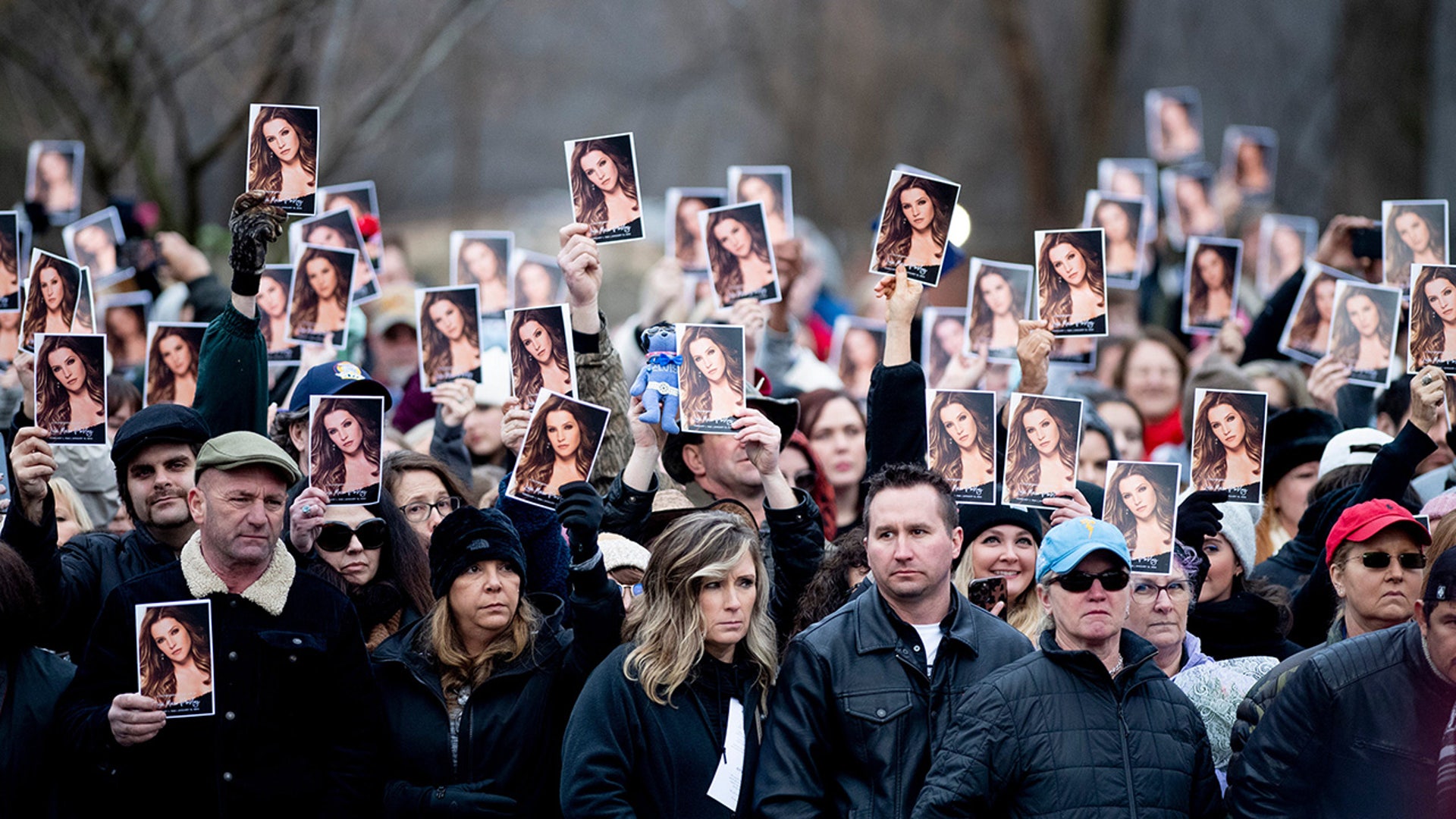 Mourners hold up a program with a photo of Lisa Marie Presley on the front lawn of Graceland