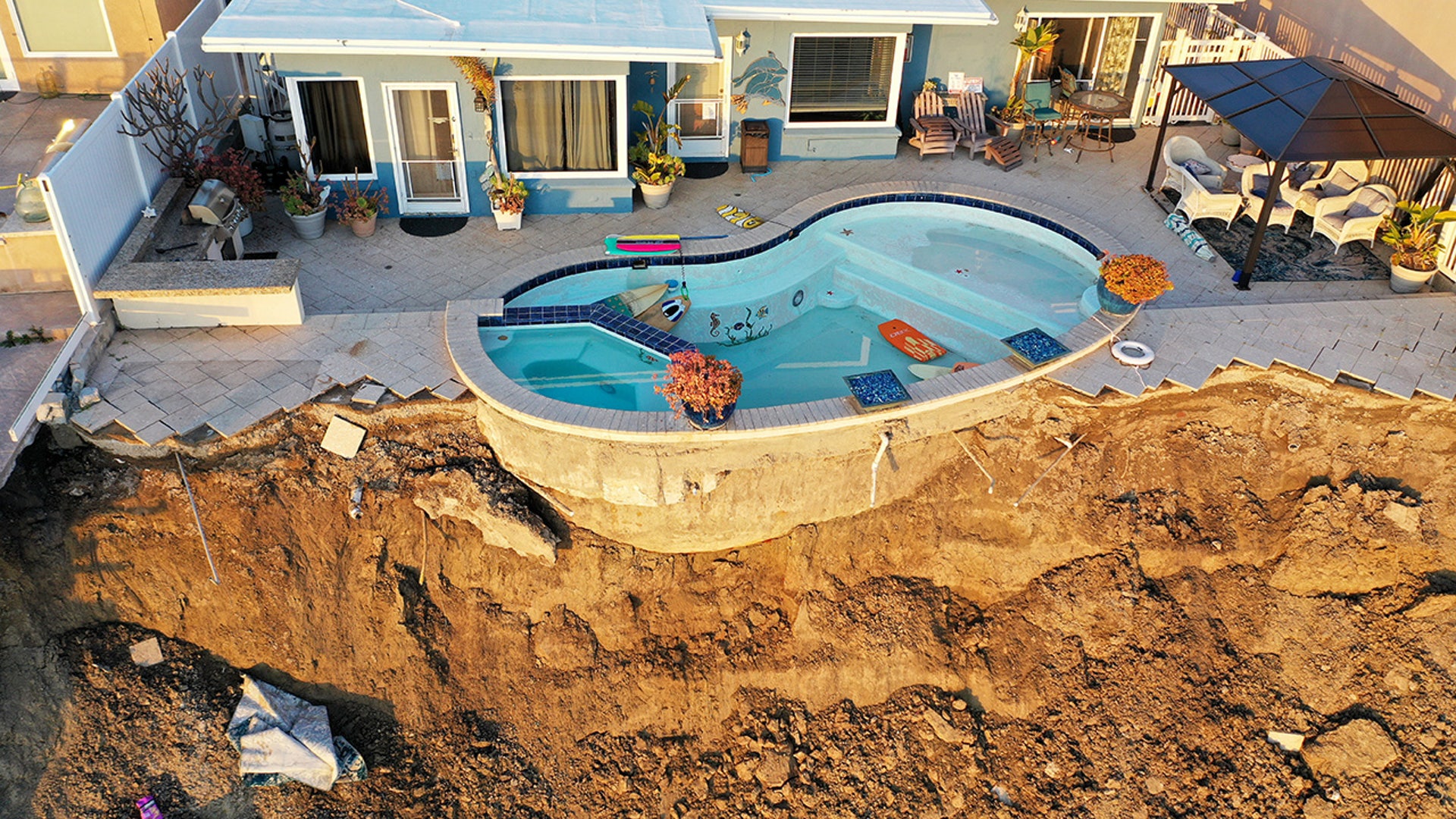 An aerial view of a remaining pool at the edge of a hillside landslide in California
