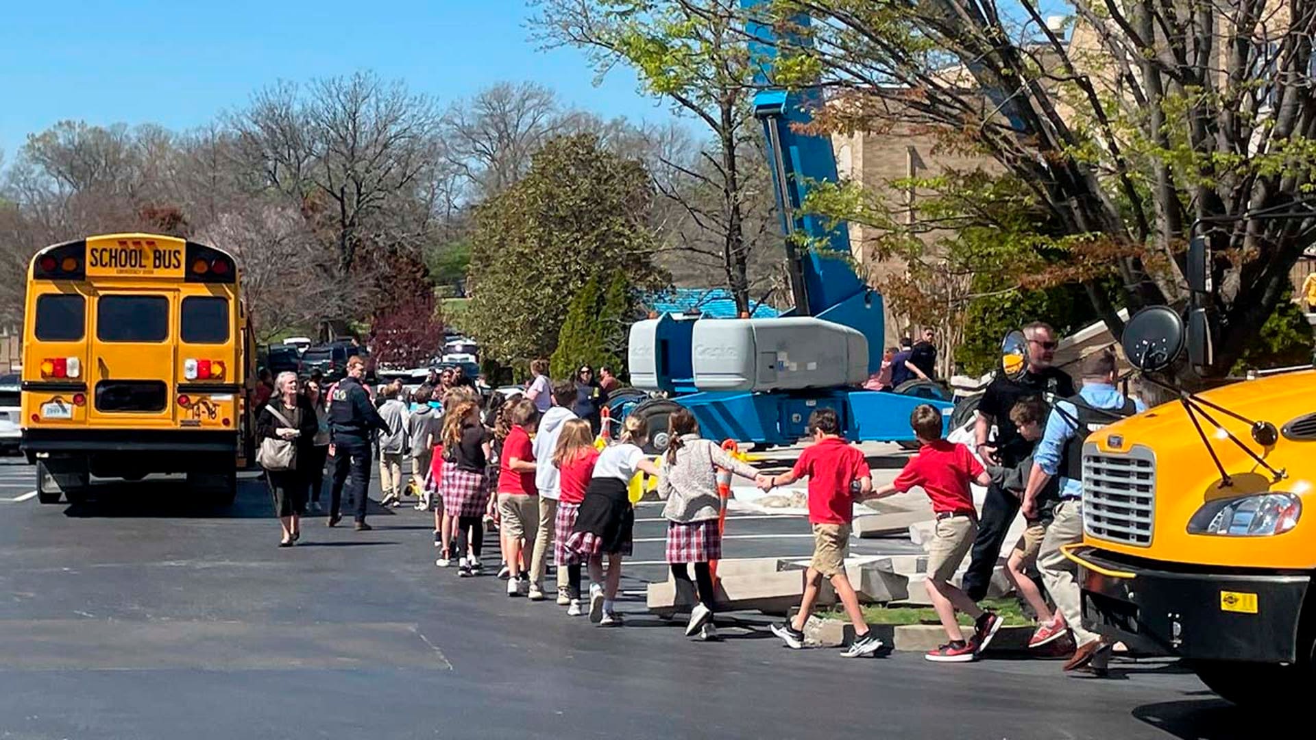 Children from The Covenant School hold hands as they are taken to a reunification site after a mass shooting