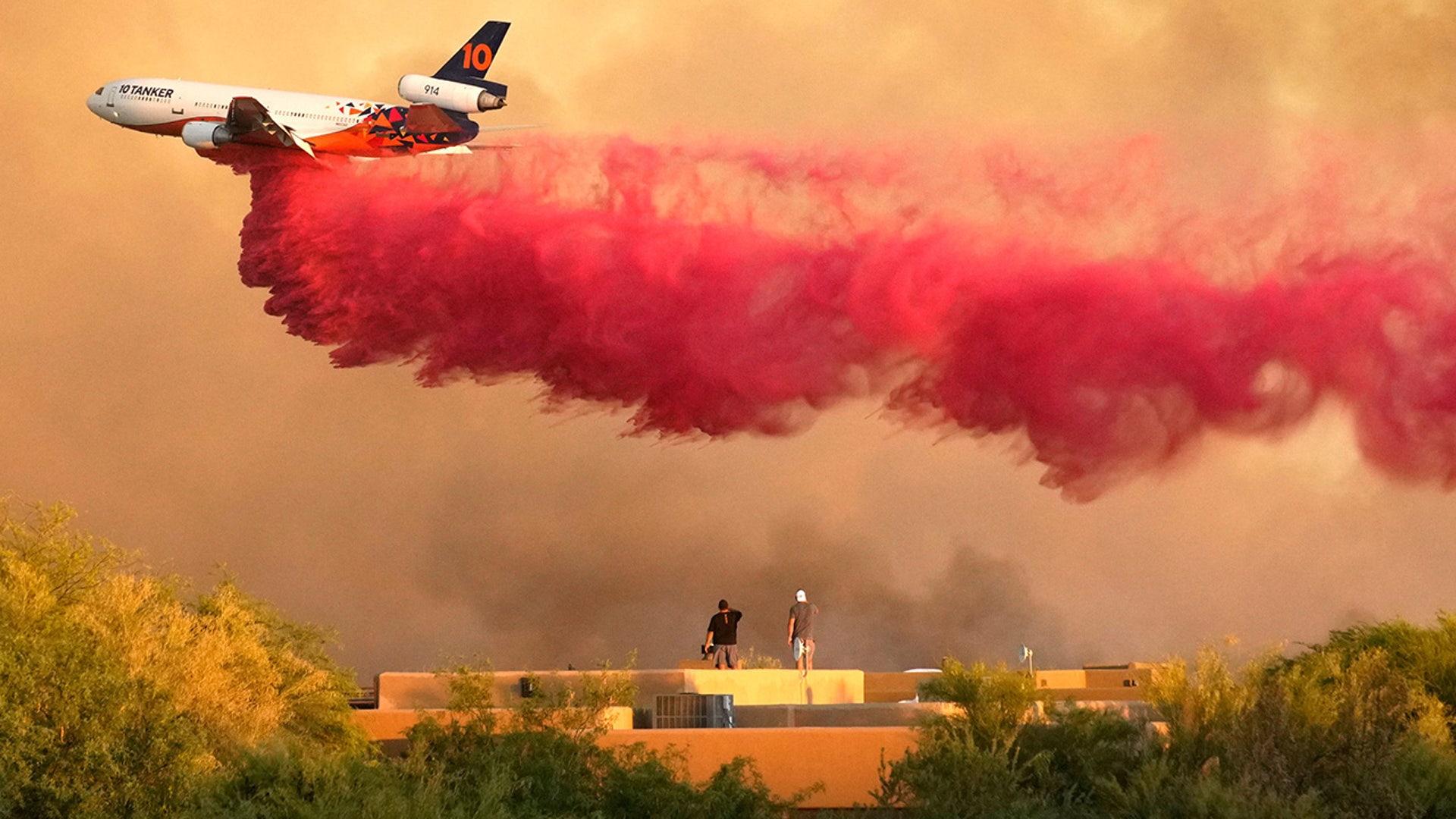 Residents stand on their roof as a DC-10 Air Tanker drops fire retardant