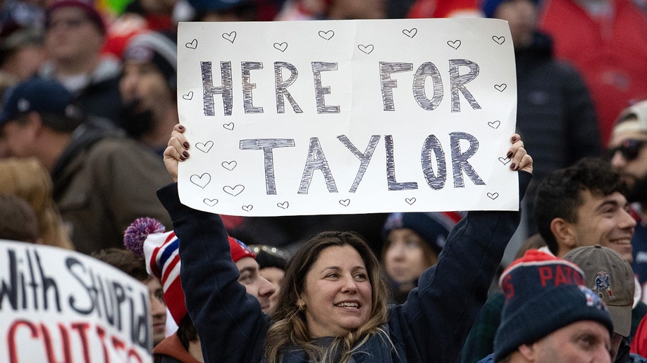 One woman holds a sign that says "HERE FOR TAYLOR" in the crowd at Gillette Stadium.
